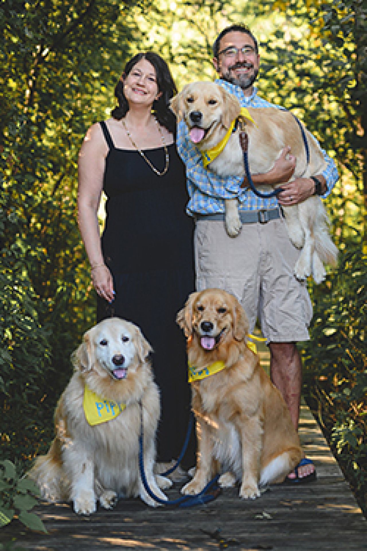 Annie and Andrew Cordo in the woods with three golden retrievers.